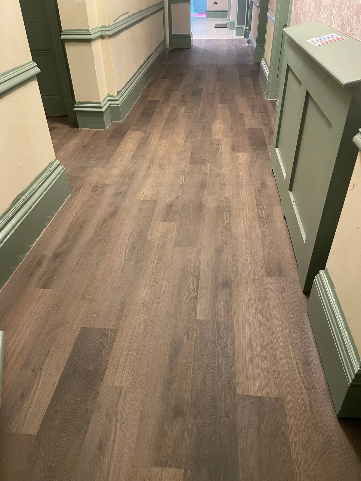 Wood effect flooring fitted through a green-panelled hallway